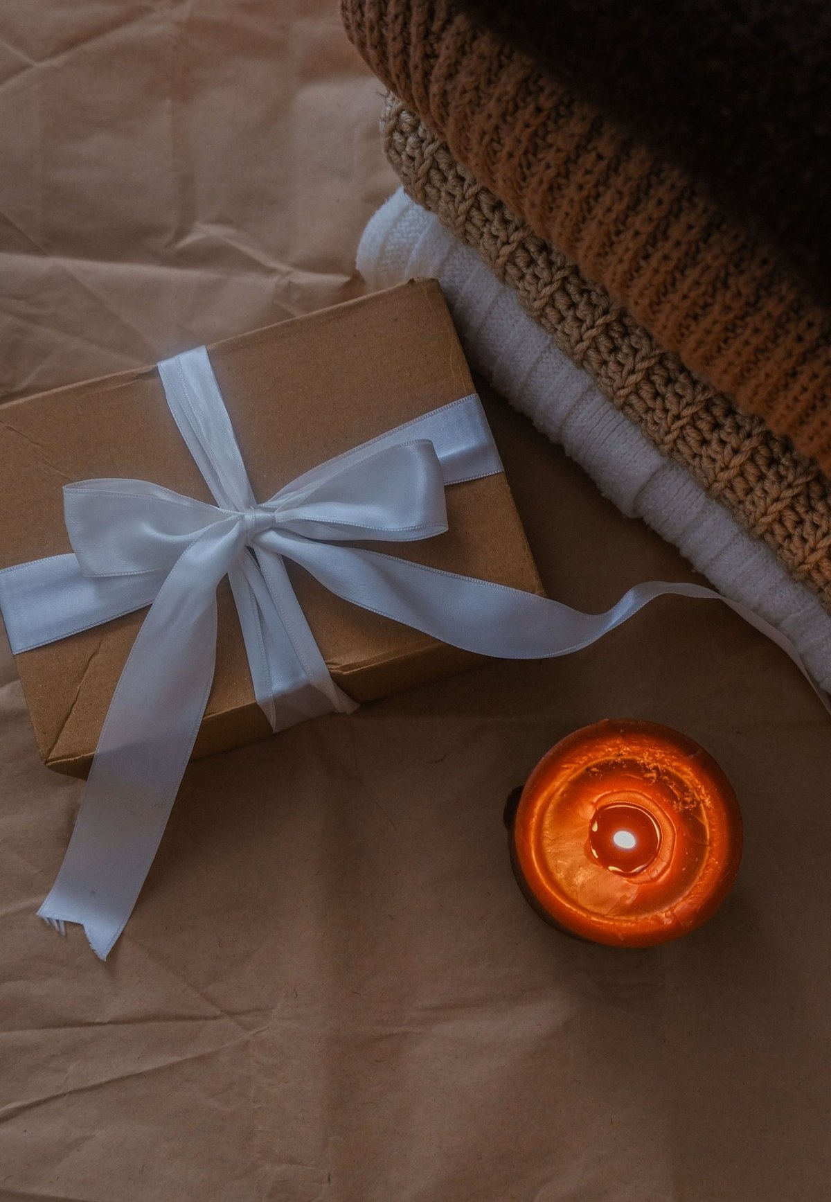 A kraft gift box with ribbon, candle and knit textiles.