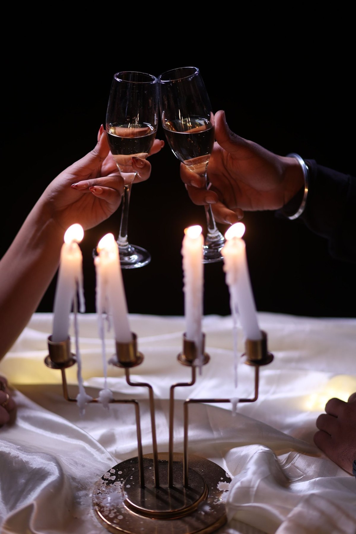 Two hands raising champagne glasses above a candelabra on a white-draped table